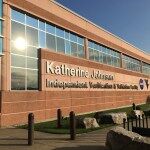 The side of a brown brick building with windows glistening in the sunlight. The words Katherine Johnson Independent Verification and Validation Facility with the NASA meatball logo and a WV for West Virginia.